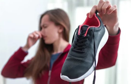 A runner holding a trainer away from her face because of the smell